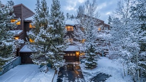 Een moderne lodge met verschillende houten huisjes, omringd door met sneeuw bedekte bomen.