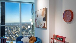 Un salon moderne avec vue sur la ville, un canapé bleu, un banc rouge et un grand tableau abstrait.
