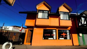Un bâtiment à deux étages avec une façade d’un orange vif, un climatiseur commercial bien visible et une enseigne sur laquelle on peut lire « LEYNA’S HOME ».