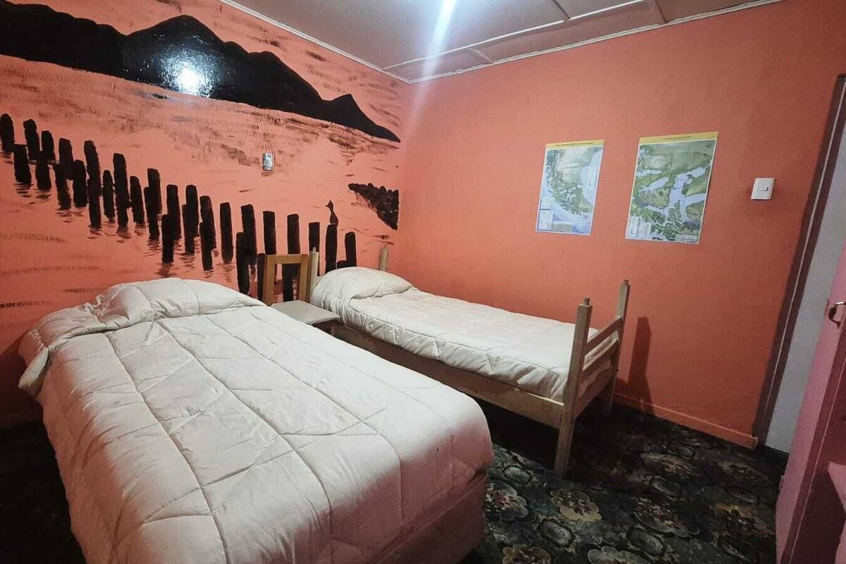 Una habitación pequeña con dos camas individuales, un mural en la pared y dos mapas colgados.
