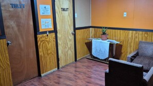 Une pièce avec des portes en bois portant l’inscription « TOILETTES », une petite table avec une plante et un fauteuil rembourré.
