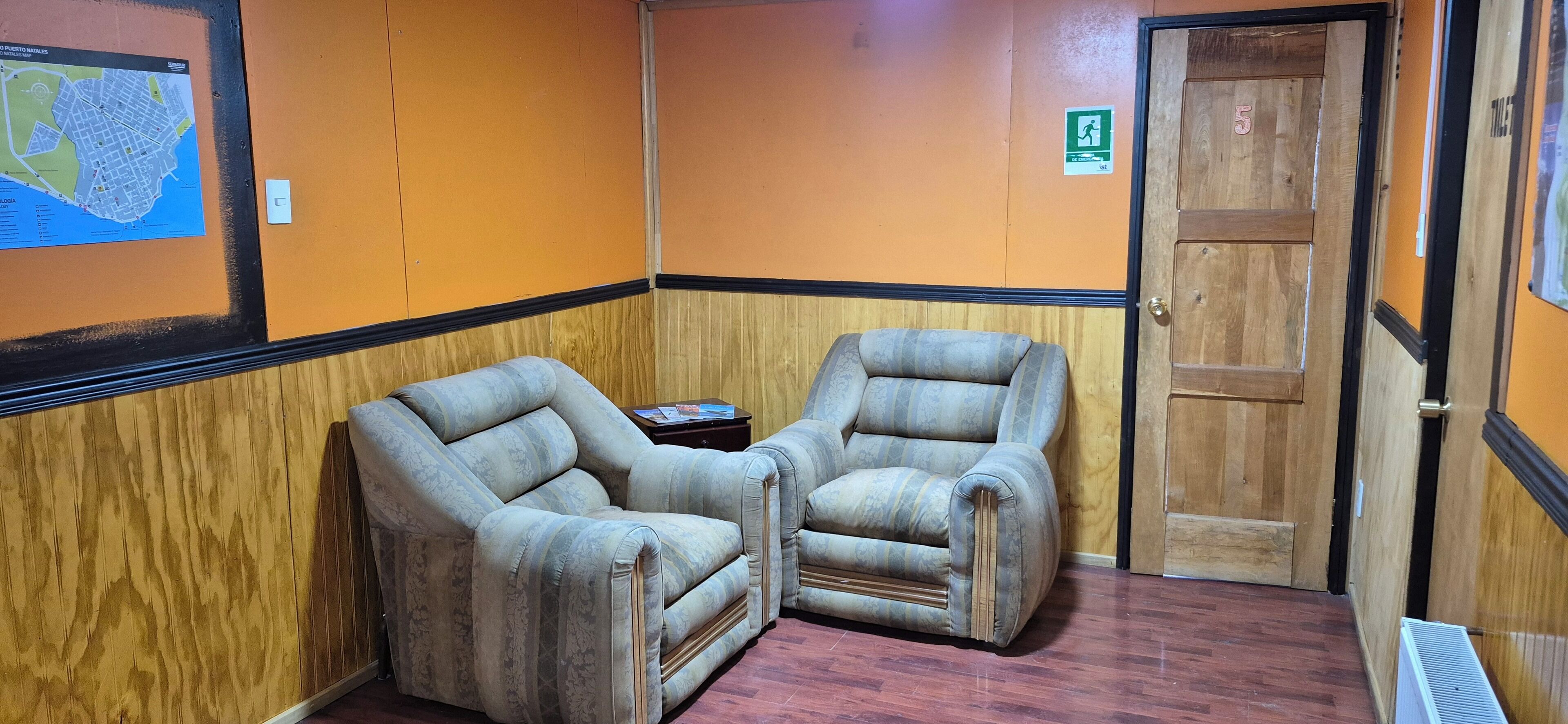 A room with two armchairs, a small table, a wooden door, and a map on the wall.