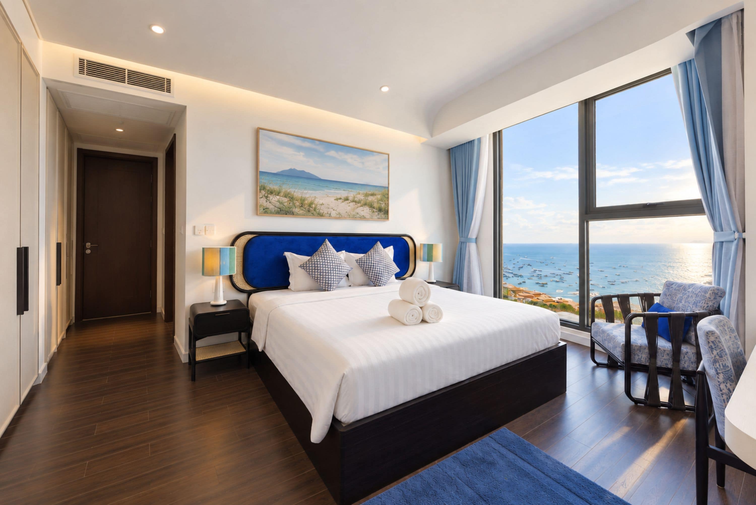 A modern bedroom with a large bed, a view of the sea, and a door leading to another room.