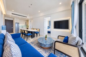 A modern living room with a blue sofa, a round coffee table, and a flat-screen TV mounted on the wall. - Skywave Apartment Firework Delight (Phu Quoc)