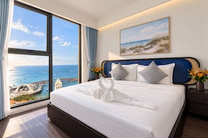 A hotel room with a large window offering a view of the sea and a pier, a neatly made bed with a towel, and a painting of a beach scene. - Skywave Apartment Firework Delight (Phu Quoc)