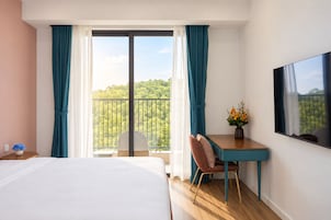 Habitaci ón de hotel con cama, escritorio, silla, televisión y balcón con vista a árboles.