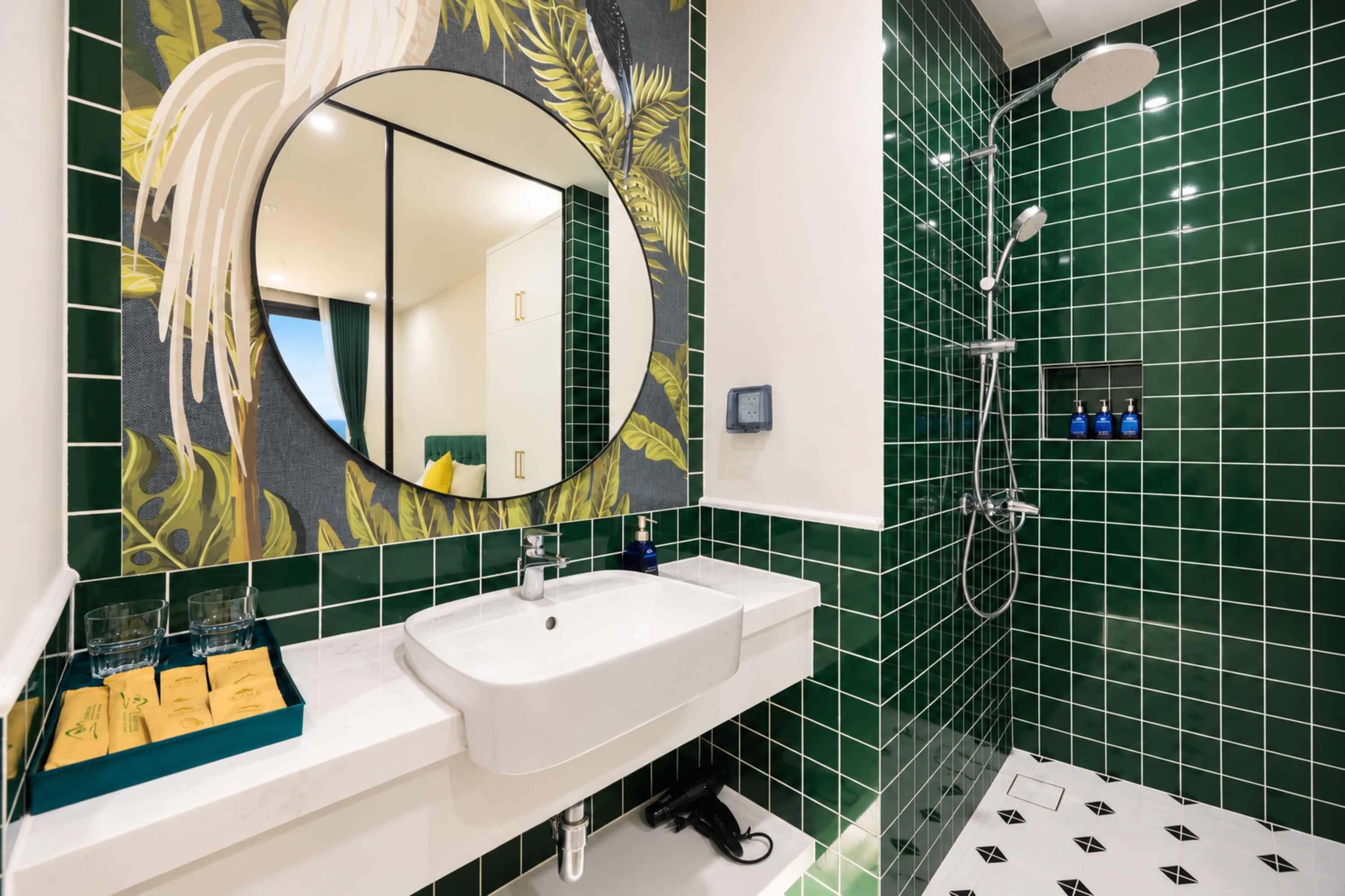 Un baño con lavamanos blanco, un espejo y una ducha con azulejos verdes.