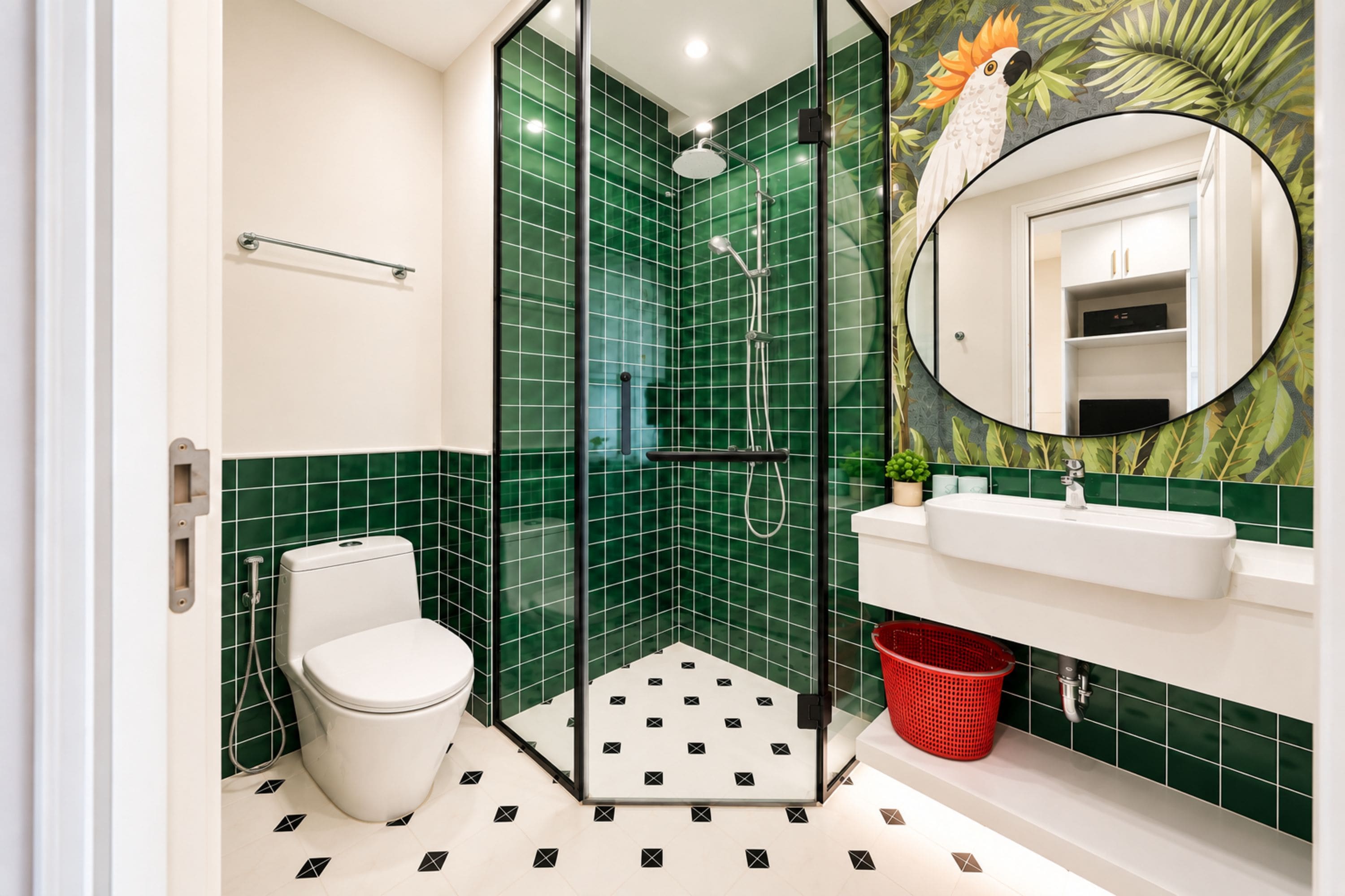 A bathroom with a glass-enclosed shower, a toilet, a sink with a mirror, and a red basket.