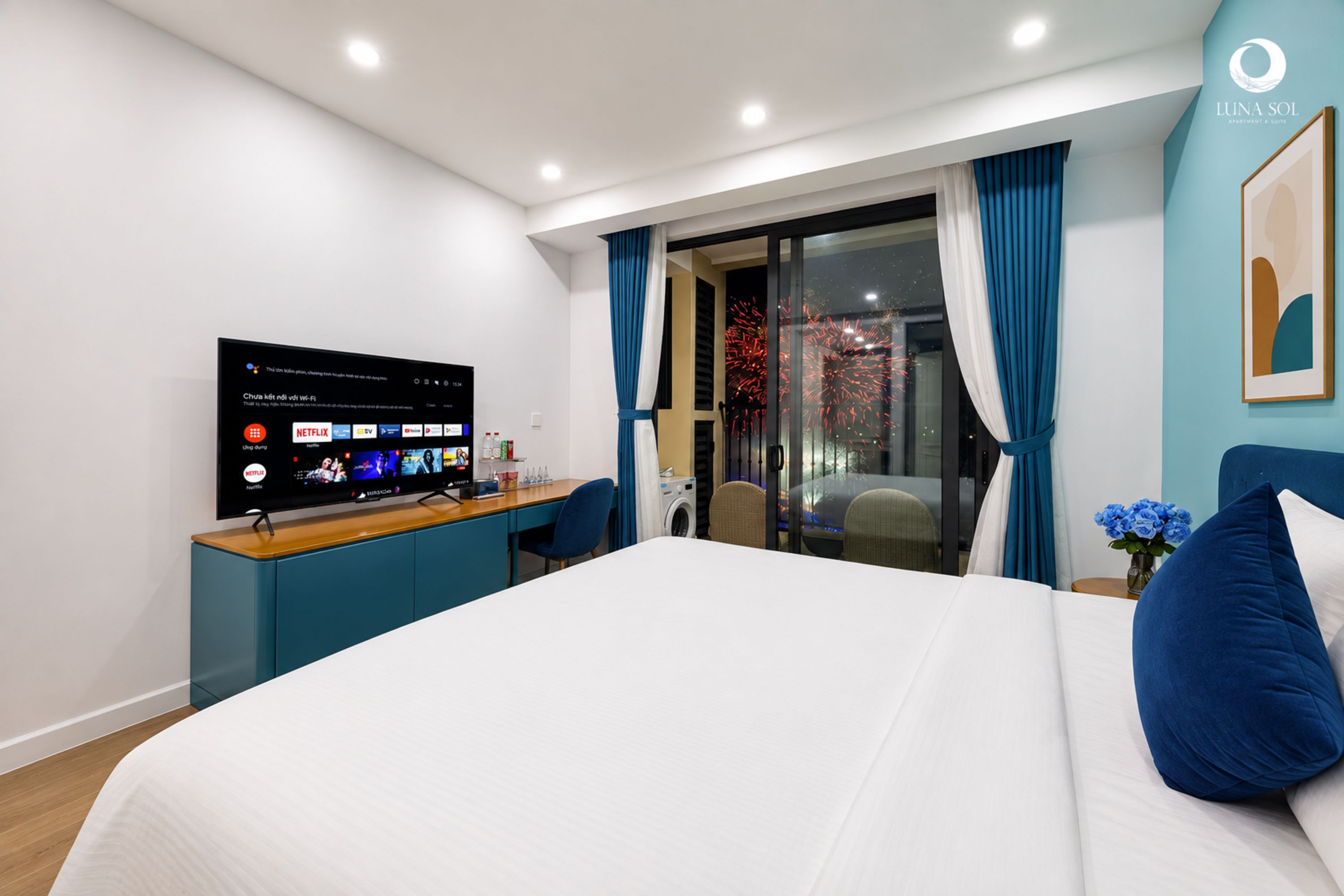 Habitación de hotel moderna con cama, escritorio, televisor de pantalla plana, ventana con cortinas y una obra de arte colgada en la pared.