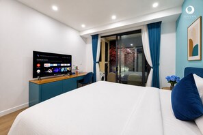 A modern hotel room with a bed, a desk with a flat-screen TV, a window with curtains, and a wall-mounted artwork. - Skywave Apartment Firework Delight (Phu Quoc)