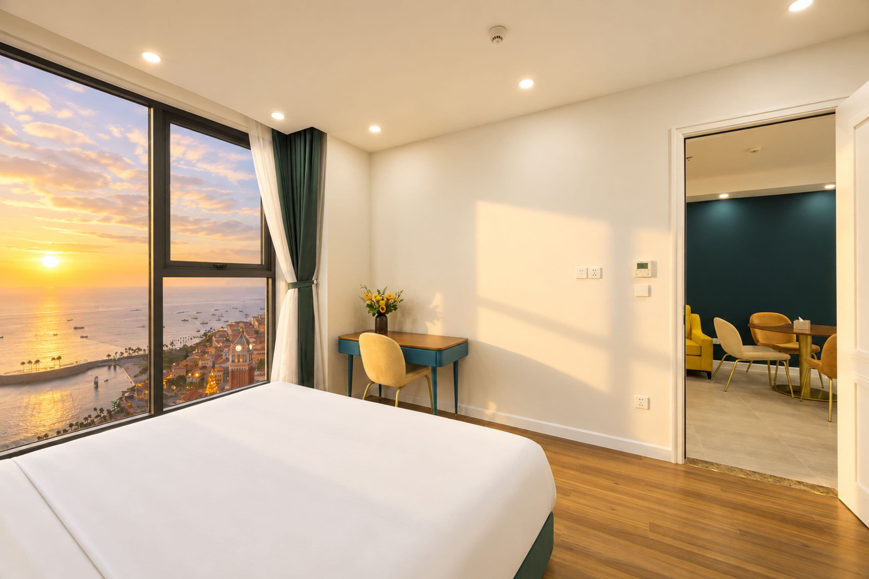 A hotel room with a large bed, a desk, and a view of the sea at sunset.