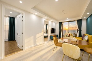 A modern living room with a dining area, a TV, and a balcony with a sunset view. - Skywave Apartment Firework Delight (Phu Quoc)