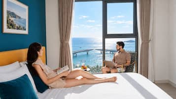 Una habitación con una cama grande, vistas al mar y un ordenador portátil sobre una silla.