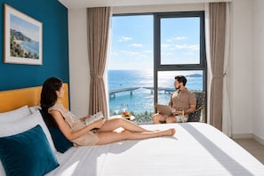 A room with a large bed, a view of the sea, and a laptop on a chair. - Skywave Apartment Firework Delight (Phu Quoc)