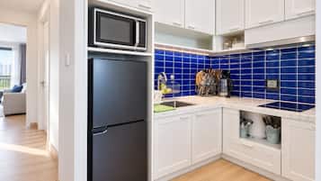 Cozinha moderna com armários brancos, geladeira preta, micro-ondas e painel de azulejos azuis.