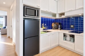 Een moderne keuken met witte kastjes, een zwarte koelkast, een magnetron en een blauwe tegelachtergrond.