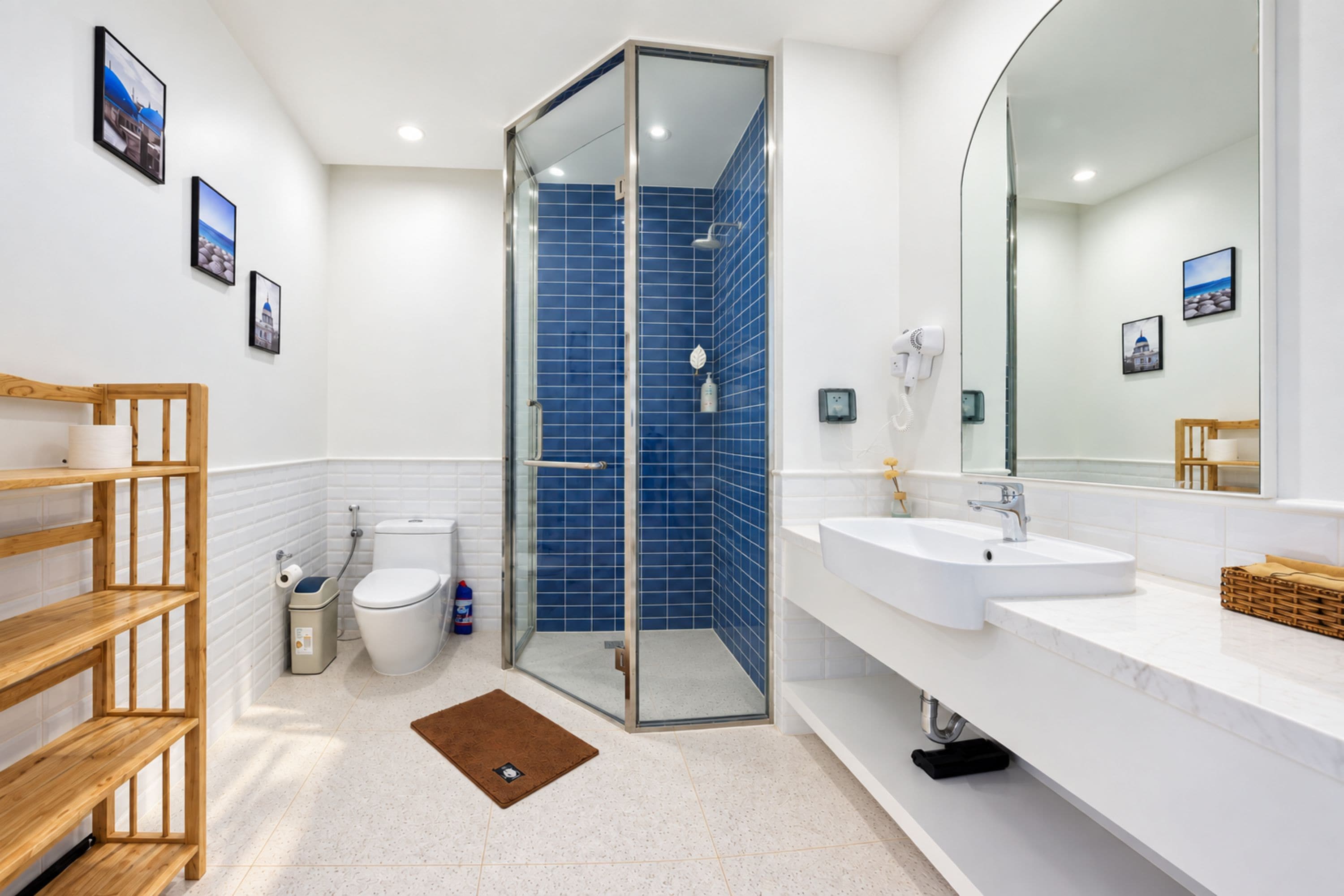 A modern bathroom with a glass shower enclosure, white fixtures, and a wooden shelf.