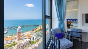 A hotel room with a large window offering a view of a coastal cityscape, including a prominent tower and the sea. - Skywave Apartment Firework Delight (Phu Quoc)