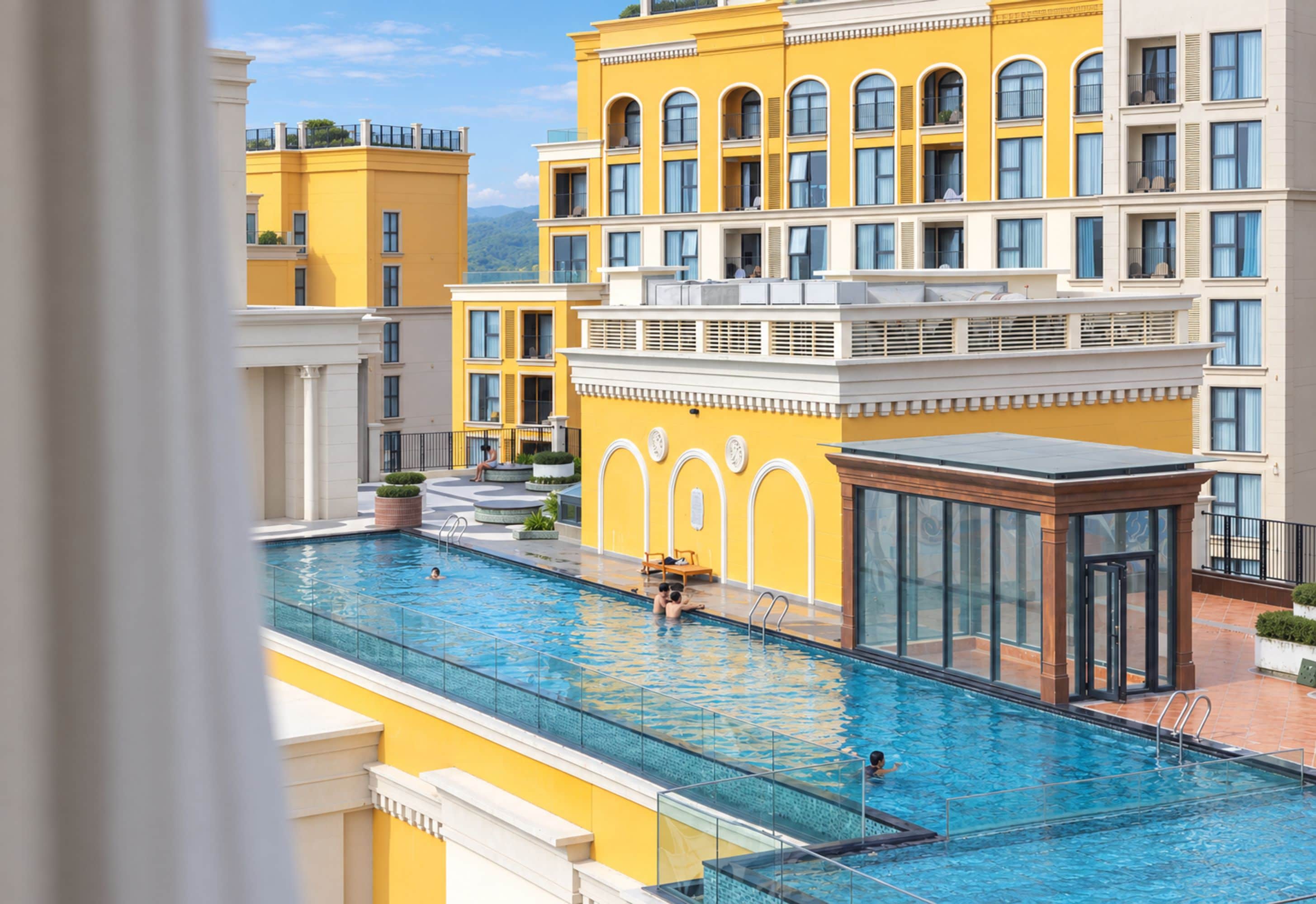 A swimming pool with a glass enclosure, surrounded by yellow buildings with multiple balconies.