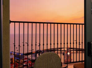 A balcony with a view of the sea at sunset, a wicker chair, and a table with a clock. - Skywave Apartment Firework Delight (Phu Quoc)