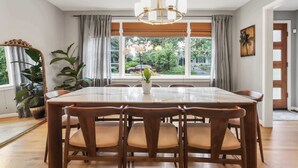 A dining area with a large table, wooden chairs, a chandelier, and large windows with curtains. - Sojourn Beautiful Home with Beach Access & Backyard (Falls Church)