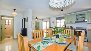 A dining area with a wooden table set for four, surrounded by chairs. There is a ceiling fan, a potted plant, and a modern light fixture above the table. - Newly renovated condo in El Cortecito in Punta Cana, Dominican Republic! (Punta Cana)