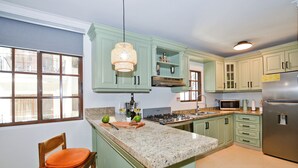 A kitchen with green cabinets, a granite countertop, a stainless steel refrigerator, and a hanging light fixture. - Newly renovated condo in El Cortecito in Punta Cana, Dominican Republic! (Punta Cana)