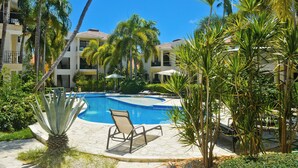 A pool area with a chair, palm trees, and a building in the background. - Newly renovated condo in El Cortecito in Punta Cana, Dominican Republic! (Punta Cana)