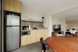 A modern kitchen with a built-in refrigerator, microwave, and oven. There is a wooden dining table with chairs and a TV in the adjacent living area.