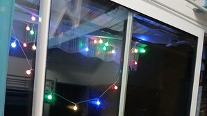 Ett rum med en skjutdörr av glas, en säng och ett väl synligt fönster dekorerat med färgglada ljusslingor.