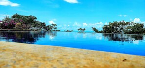 An infinity pool with clear blue water, surrounded by lush greenery and trees. - 3-bedroom villa in beautiful Hatillo with AC (Hatillo)