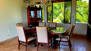Un coin repas comprenant une table et des chaises en bois, un buffet et de grandes fenêtres donnant sur un paysage verdoyant.