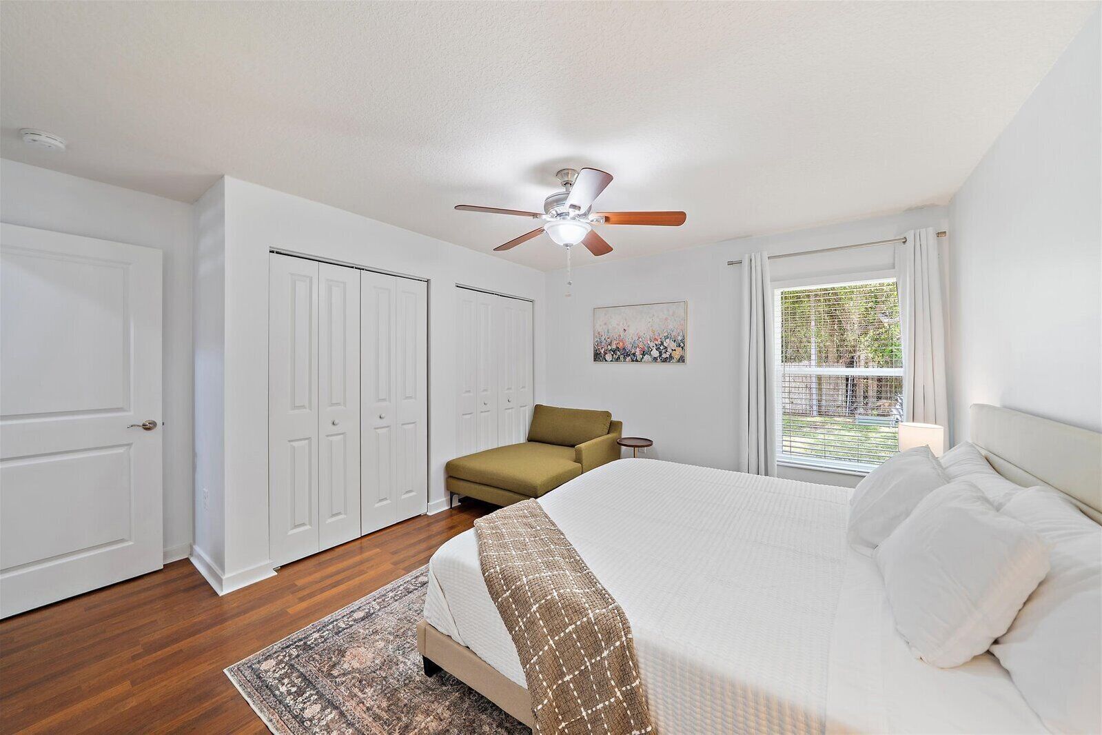 A bedroom with a bed, a ceiling fan, a window with blinds, and a door.