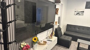 A modern living room with a large flat-screen TV mounted on a black wall, a grey sofa, a white console table with decorative items, and a wooden floor. - ZEVEN HOUSE - CUSCO APARTMENT (Cusco)