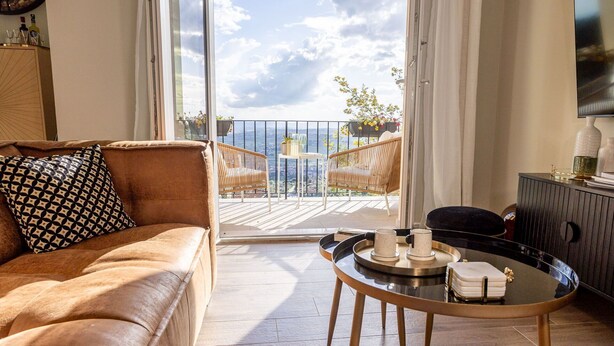 A living room with a brown leather sofa, a round coffee table with decorative items, and a balcony with wicker chairs and potted plants. - Apartment in Cortona with 3 bedrooms sleeps 6 (Cortona)