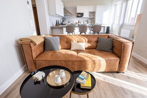 A modern living room with a brown leather sofa, two black and white patterned pillows, a black coffee table with a tray holding a white box, two cups, and a book.