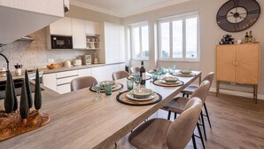 A modern kitchen with white cabinets, a dining area with a long table set for six, and a large wall clock. - Apartment in Cortona with 3 bedrooms sleeps 6 (Cortona)