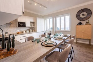 A modern kitchen with white cabinets, a dining area with a long table set for six, and a large wall clock.