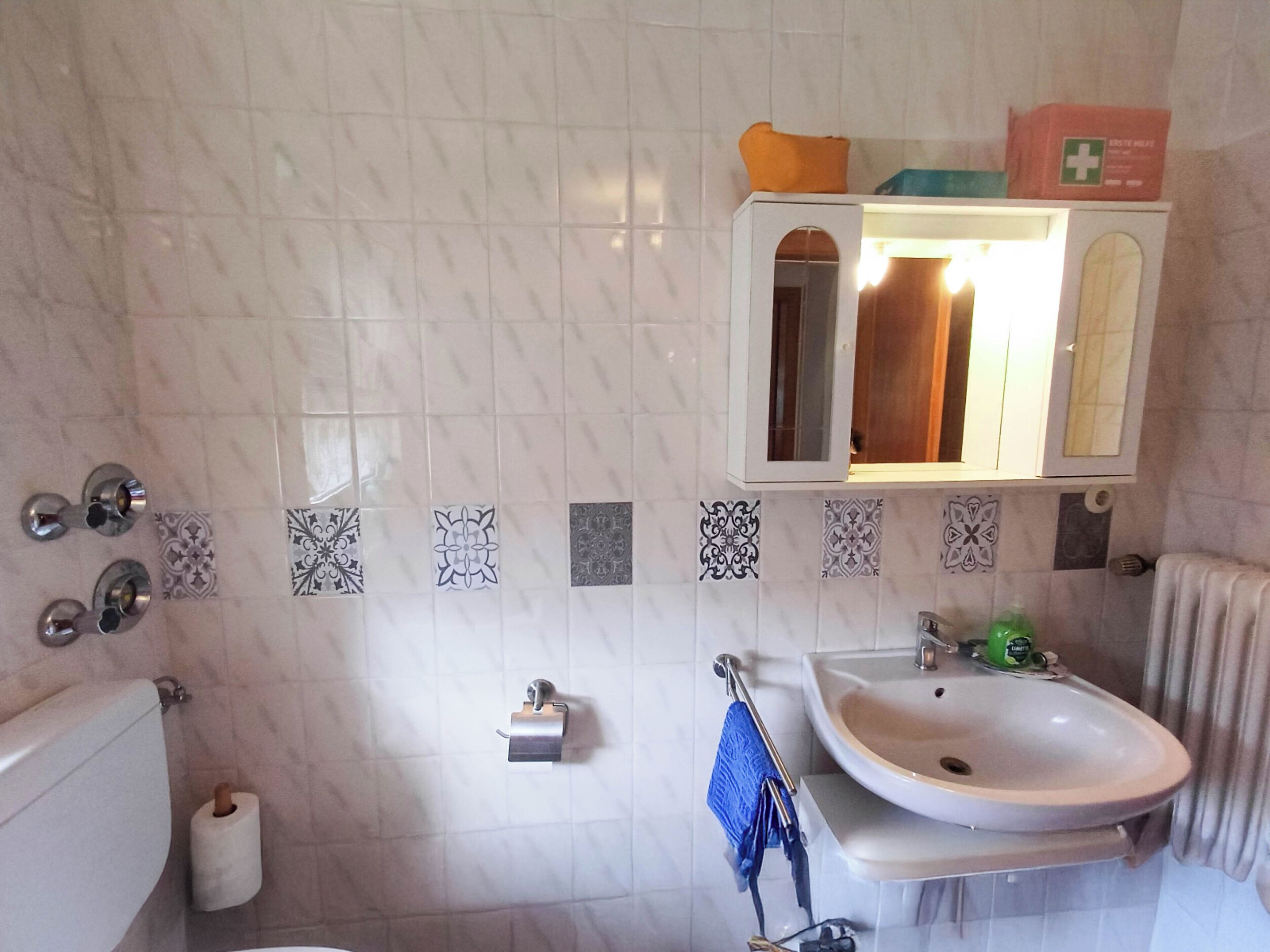 Ein Badezimmer mit Toilette, Waschbecken, Spiegel und gemusterten Fliesen.