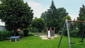A playground with swings, a slide, and a table tennis table in a grassy area with trees. - Apartment with balcony in Teutoburg Forest (Blomberg)