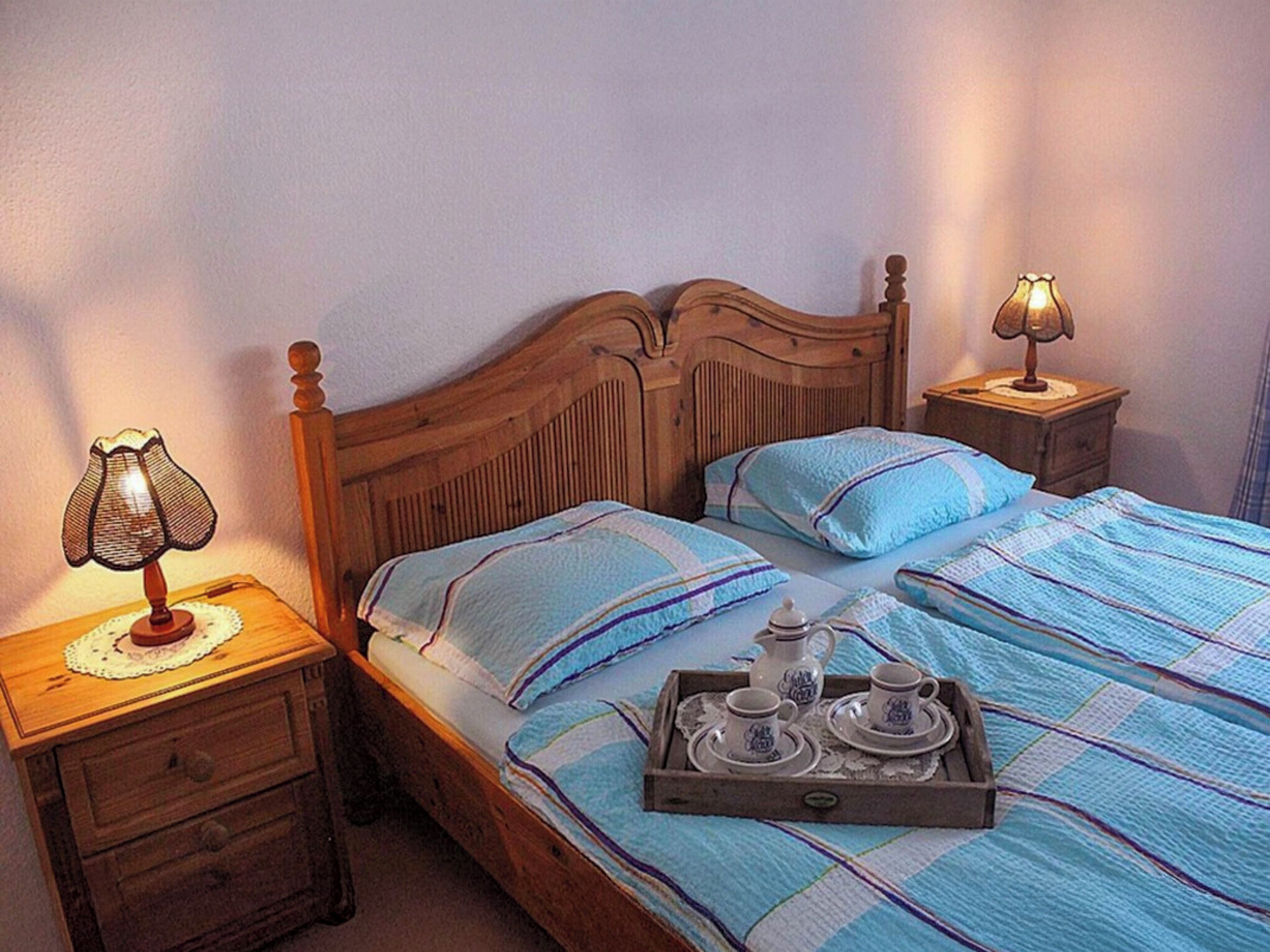 Une chambre à coucher avec un lit en bois, deux tables de chevet, une petite table, une lampe et un plateau avec des tasses à thé et une théière.
