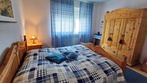 A bedroom with a wooden bed, a nightstand with a lamp, a wooden wardrobe, and a window with curtains. - Apartment with balcony in Teutoburg Forest (Blomberg)
