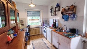 A compact kitchen with wooden cabinets, a built-in oven, a sink, and a window with blinds. - Apartment with balcony in Teutoburg Forest (Blomberg)