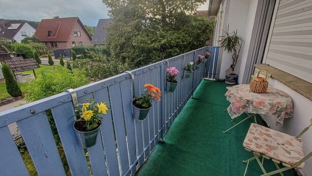 A balcony with a green artificial turf, potted plants, and a small table with a chair. - Apartment with balcony in Teutoburg Forest (Blomberg)