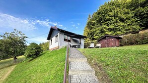 A house with a stone pathway leading to the entrance, surrounded by lush greenery and a clear sky. - Holiday home in the Thuringian Forest (Langenbach)