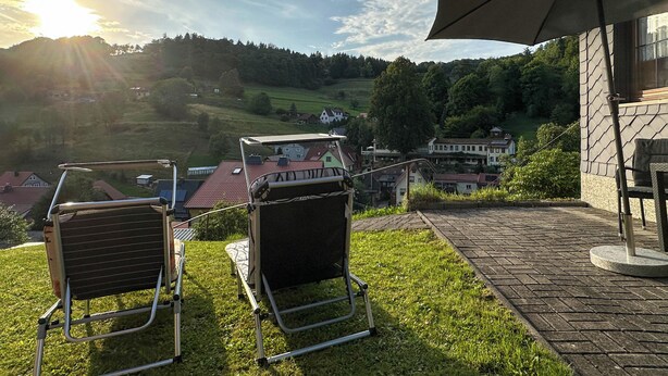 A patio with two lawn chairs, a table, and a large umbrella. - Holiday home in the Thuringian Forest (Langenbach)