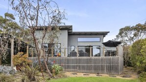 Et moderne hus med to etager, en indhegnet baghave, et stort vindue og en overdækket udendørs siddeplads.