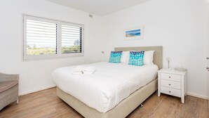 Een netjes opgemaakte slaapkamer met een bed, nachtkastje en uitzicht door het raam.