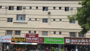 Um edifício de vários andares com diversos estabelecimentos comerciais no andar térreo, incluindo um hotel chamado "BMR Stay" e uma loja chamada "Sri Saptarshi".