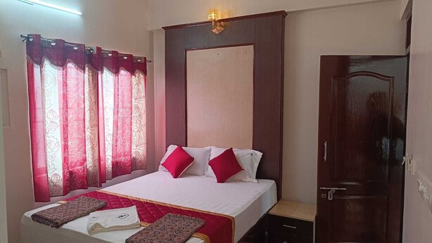 Cama bem arrumada com roupa de cama branca e vermelha, cabeceira de madeira e mesa de cabeceira com abajur.